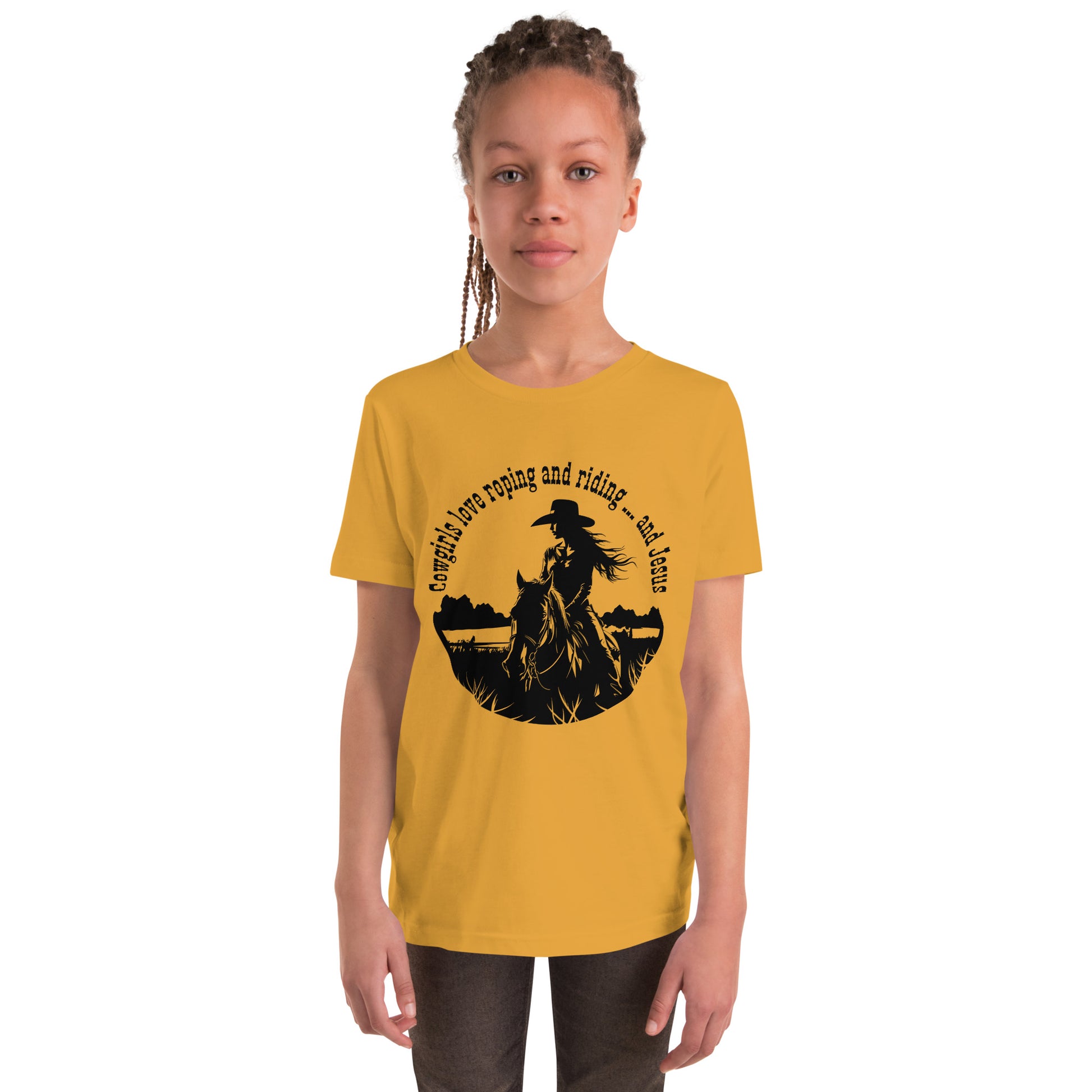 Young girl with hair pulled back in cornrows wears brown pants and a mustard-colored short-sleeved t-shirt with a circular design of a cowgirl on horseback in a grassy field that says Cowgirls love roping and riding ... and Jesus.