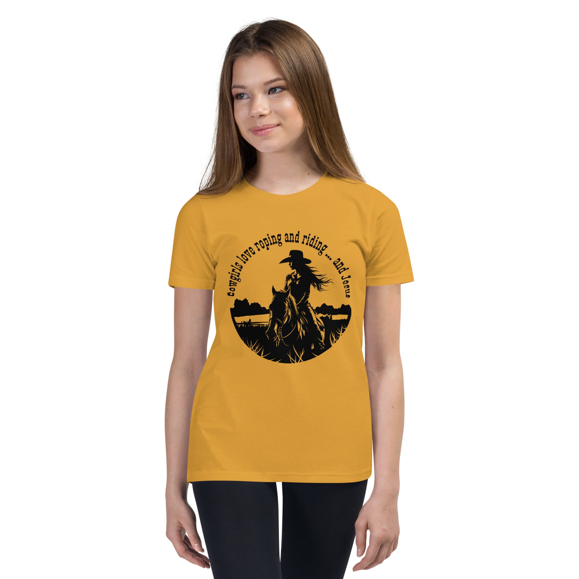 Pre-teen girl with long hair looks off-camera and she is wearing dark pants and a mustard colored shirt with a cowgirl on horseback in a circular design that says:  Cowgirls love roping and riding ... and Jesus.